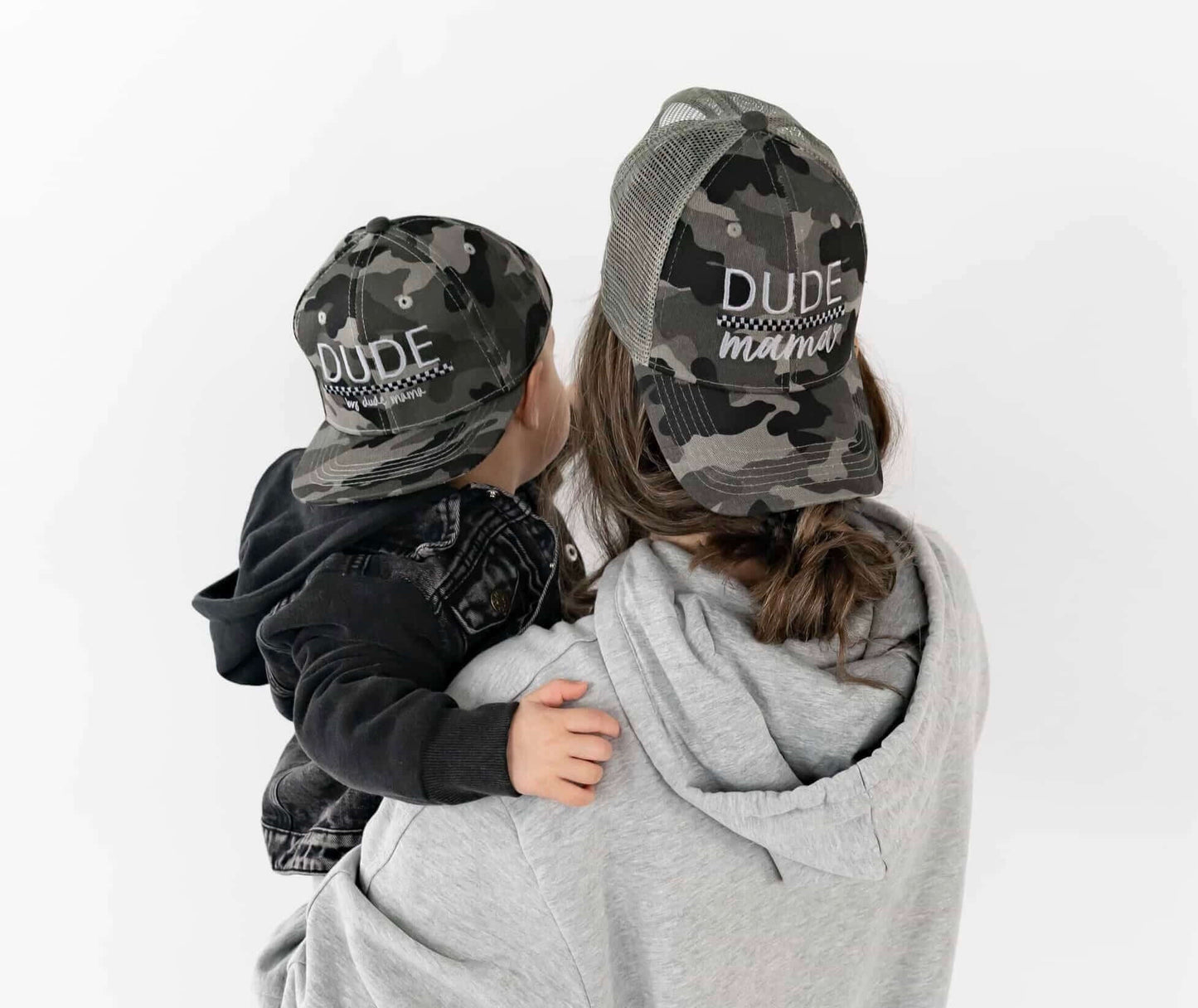 Mom holding her son and they are wearing matching mom and son hats - camo and checkered design.