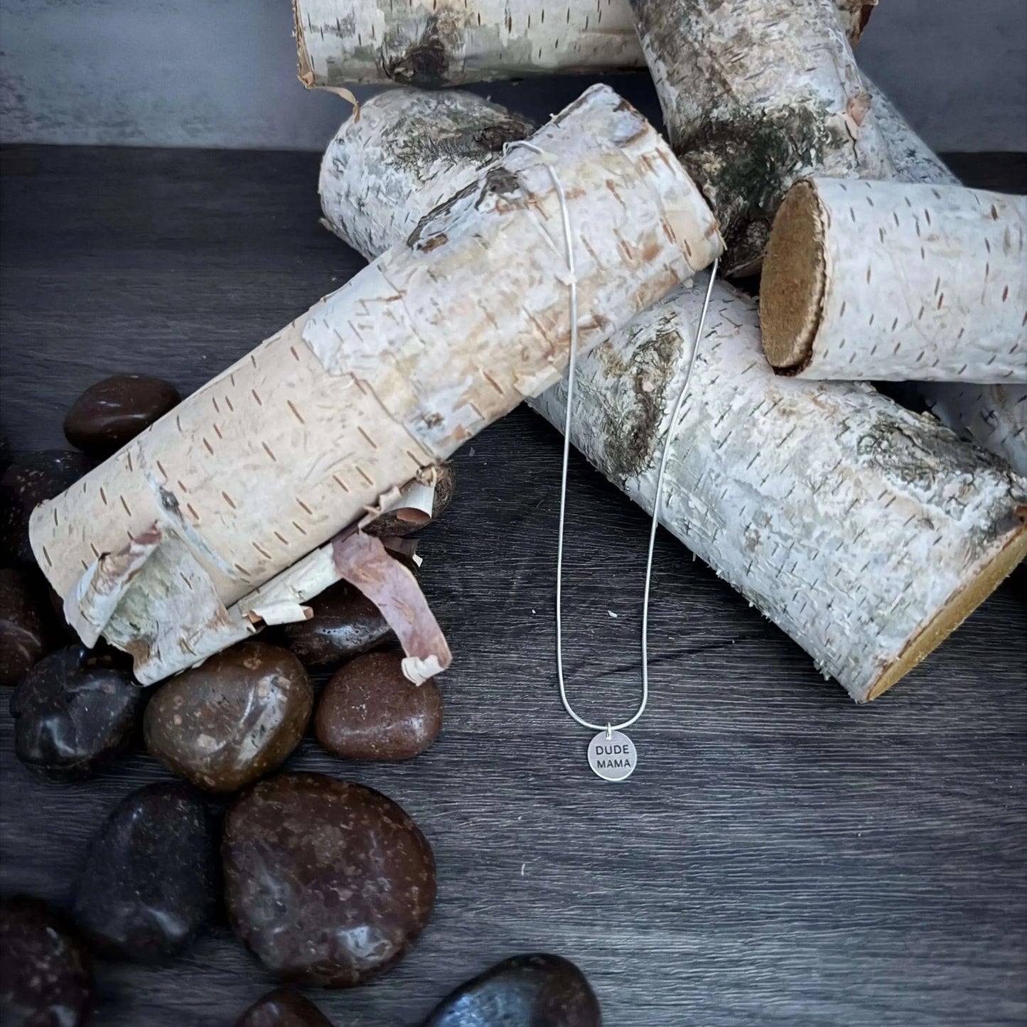 Engraved Dude Mama pendant necklace displayed on birch bark with stones, perfect for baby shower gifts