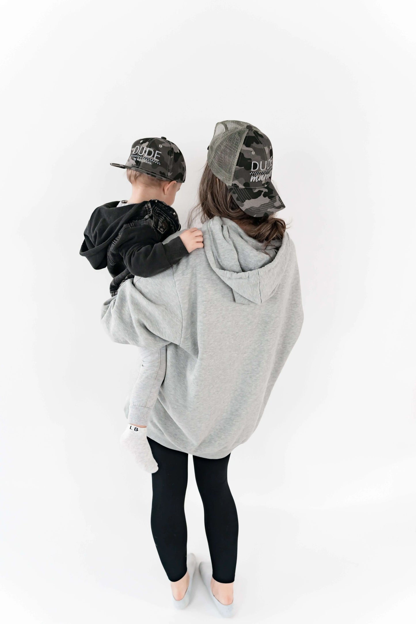 Mom holding her son and they are wearing matching mom and son hats - camo and checkered design.