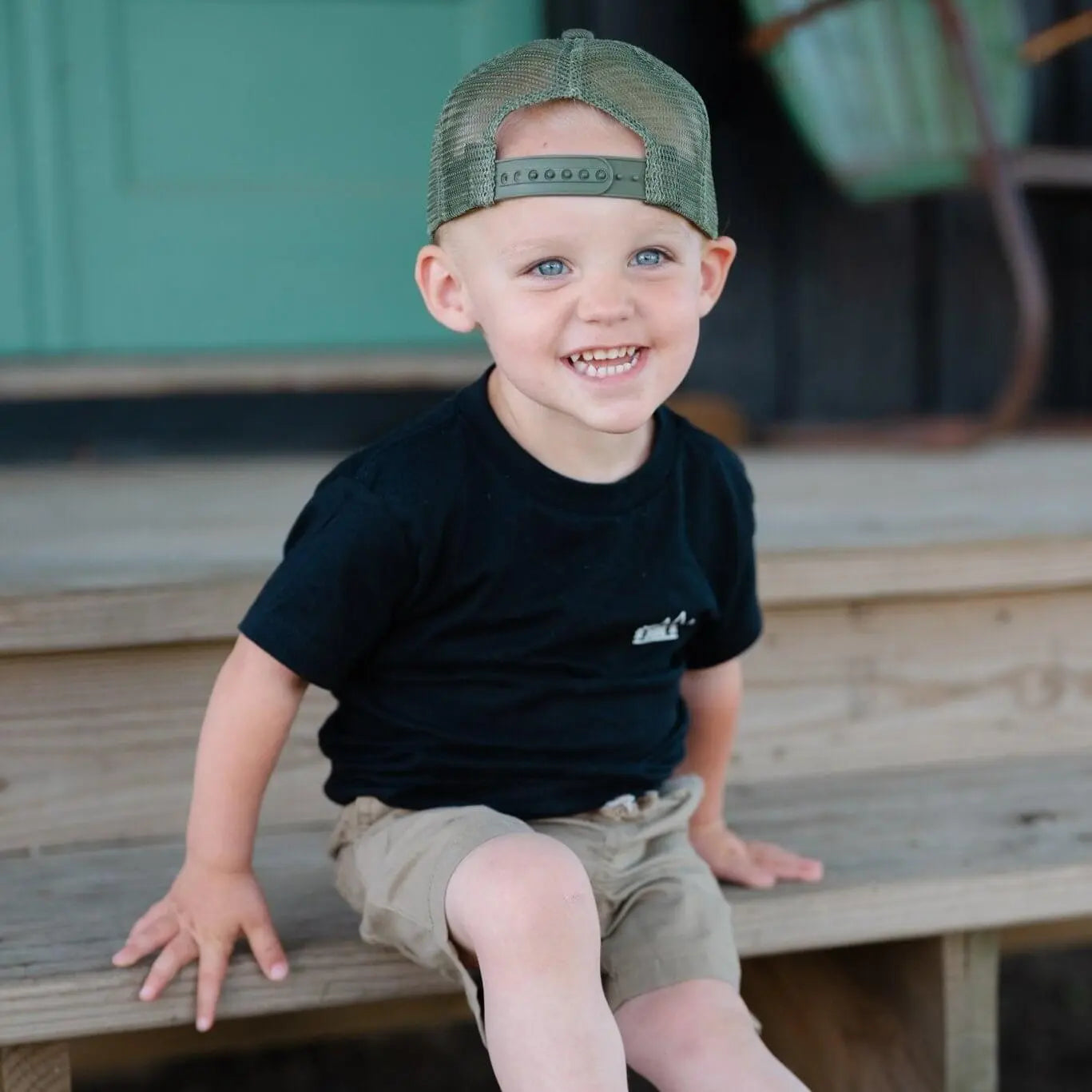 Happy boy wearing a Green Mesh Dude Hat, sitting on steps, showcasing a stylish boy hat for confident kids.