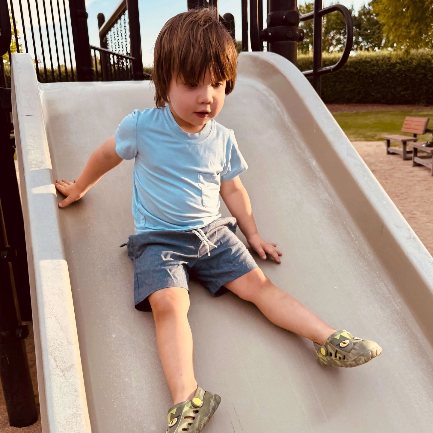 Light Blue Bamboo Boys Shirt worn by a boy sliding down a playground slide, enjoying an outdoor adventure.