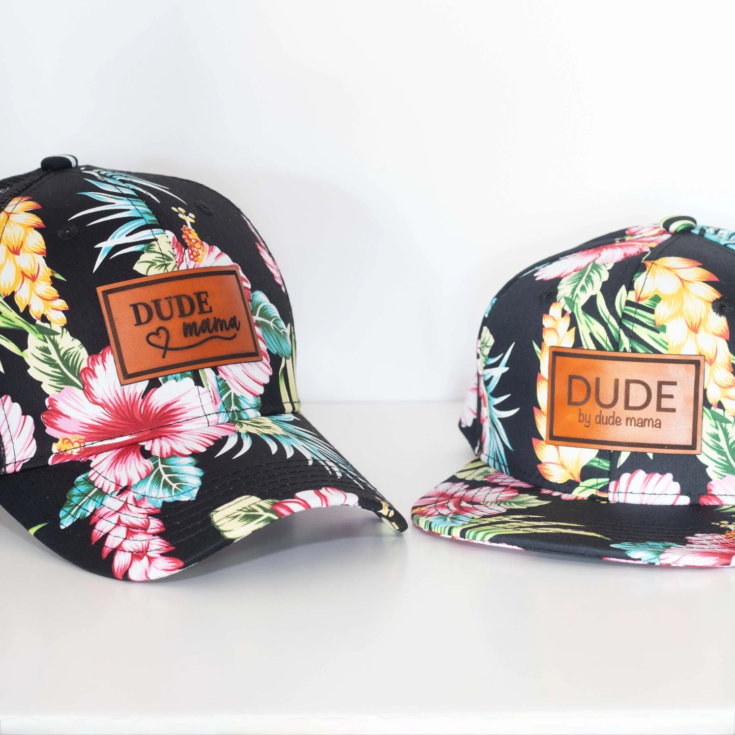 Black Hawaiian matching mom and son hats with floral designs and branded patches for Dude and Dude Mama.