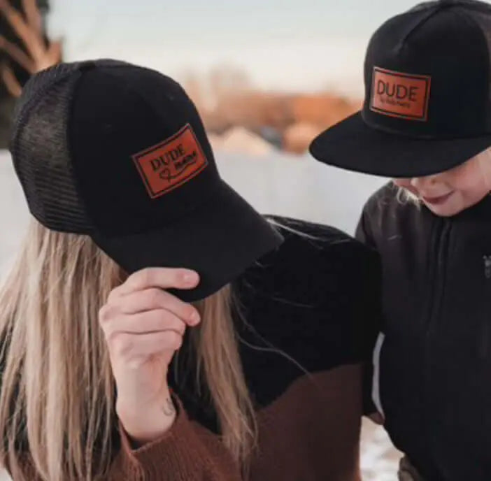 Matching hats for mama and dude, featuring black caps with leather patches, perfect for family adventures. Boy mom hat and Dude hat