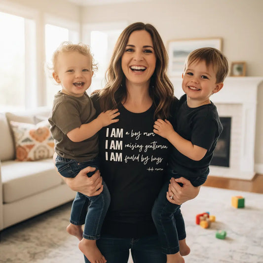 Mom smiling holding her boys and wearing a boy mom shirt that says: “I Am a Boy Mom. I Am Raising Gentlemen. I Am Fueled by Hugs."