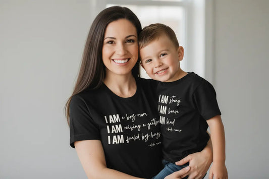 A mom holding her son. You can feel the love in this photo - they are wearing mom and son matching black shirts. It is an adorable mom and son matching outfit. The text on both shirts is off white. Mama's shirt says 'I am a boy mom, I am raising a gentleman, I am fueled by hugs.' Her son's shirt says 'I am strong, I am brave, I am kind.'