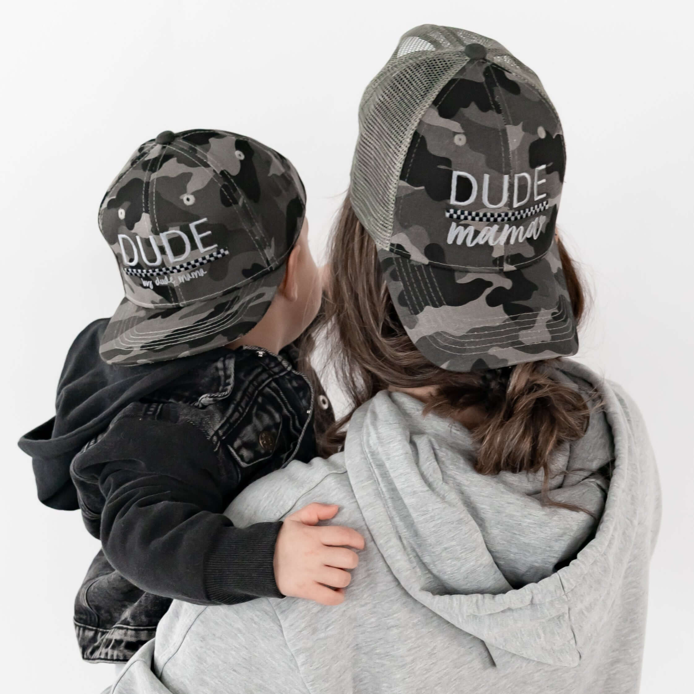 Mom holding her son and they are wearing matching mom and son hats - camo and checkered design.