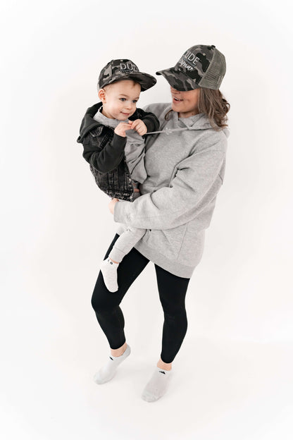 Mom holding her son and they are wearing matching mom and son hats - camo and checkered design. 