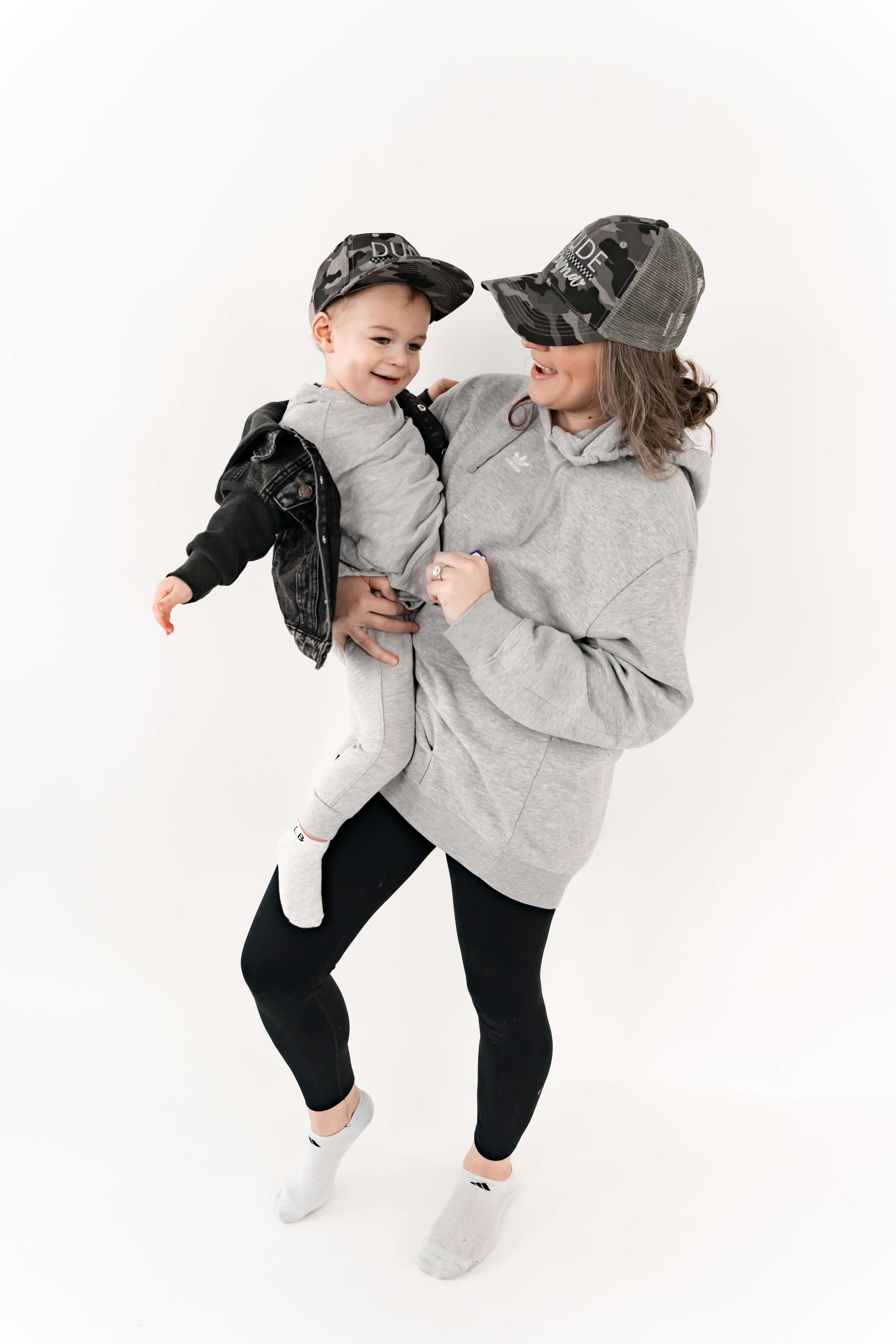 Mom holding her son and they are wearing matching mom and son hats - camo and checkered design. 