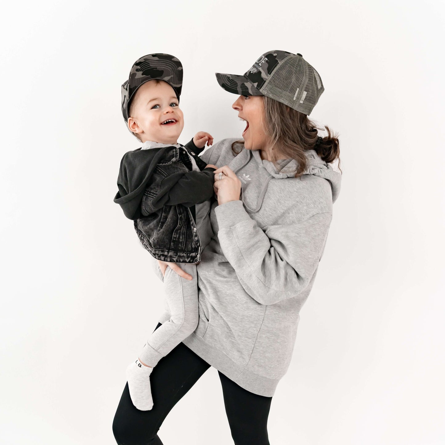 Mom holding her son and they are wearing matching mom and son hats - camo and checkered design. 