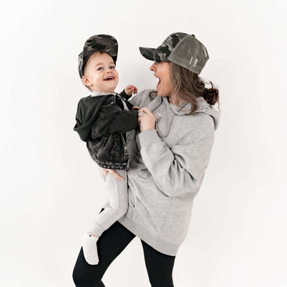 Mom holding her son and they are wearing matching mom and son hats - camo and checkered design. 