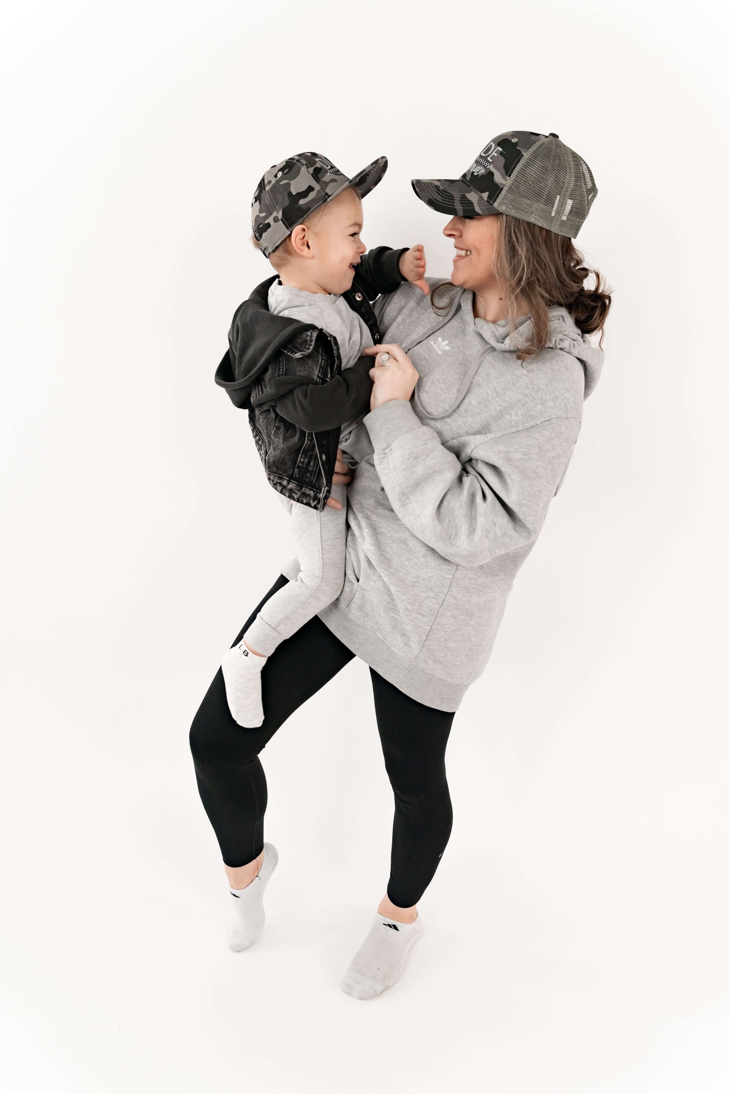 Mom holding her son and they are wearing matching mom and son hats - camo and checkered design. 