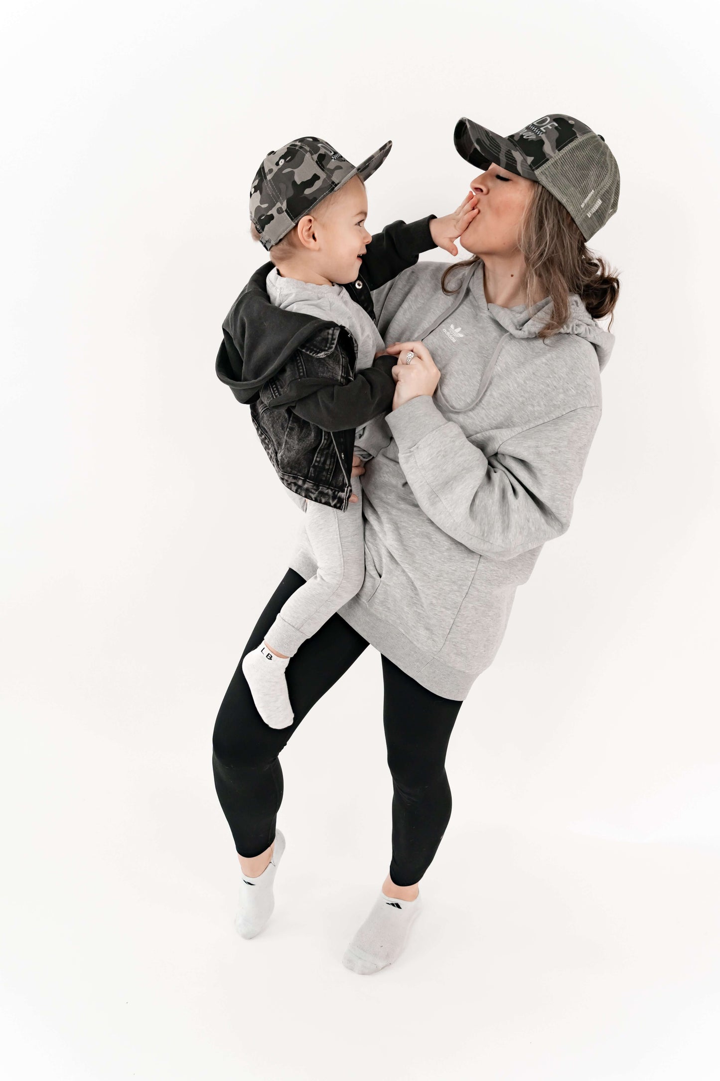 Mom holding her son and they are wearing matching mom and son hats - camo and checkered design. 