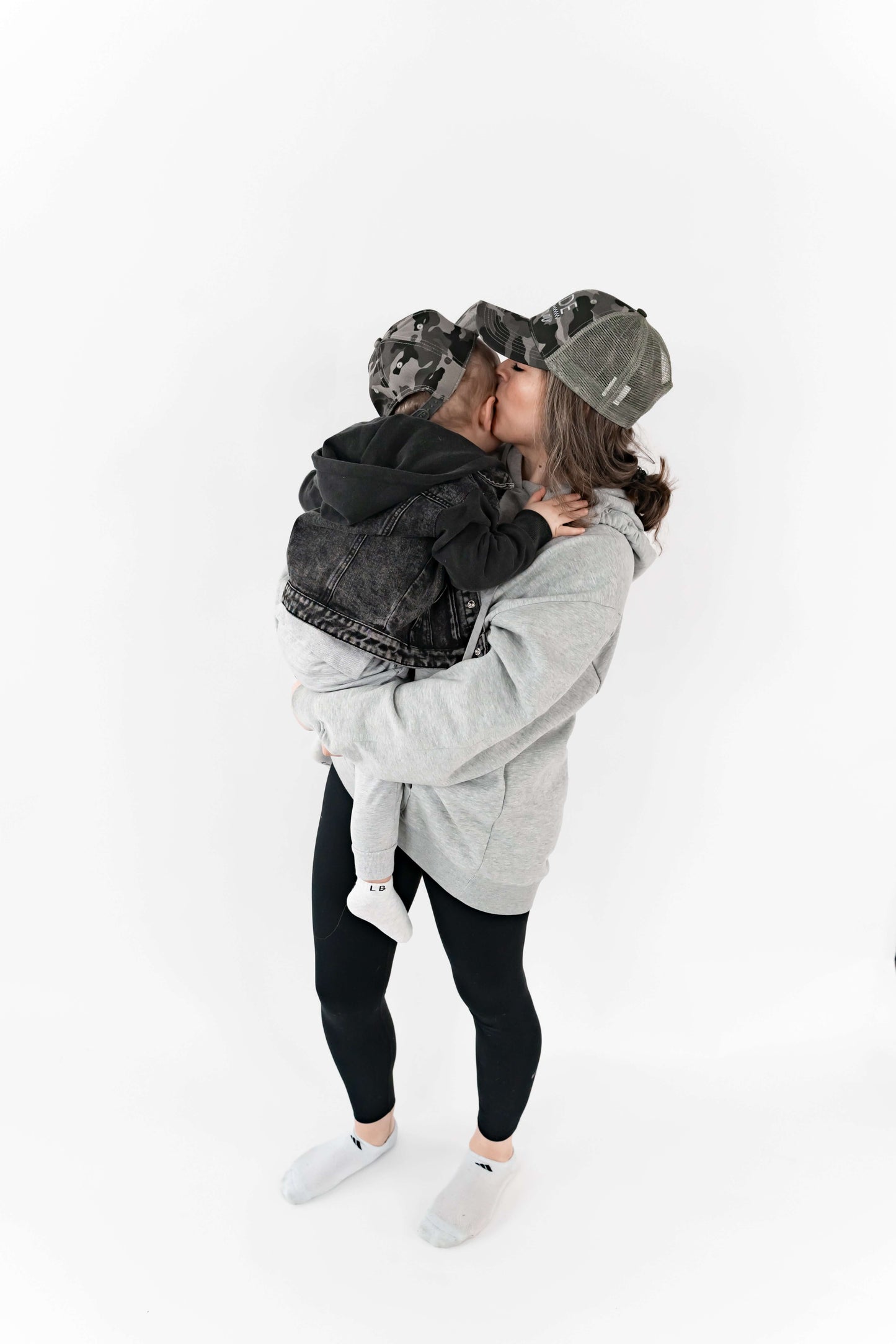 Mom holding her son and they are wearing matching mom and son hats - camo and checkered design. 