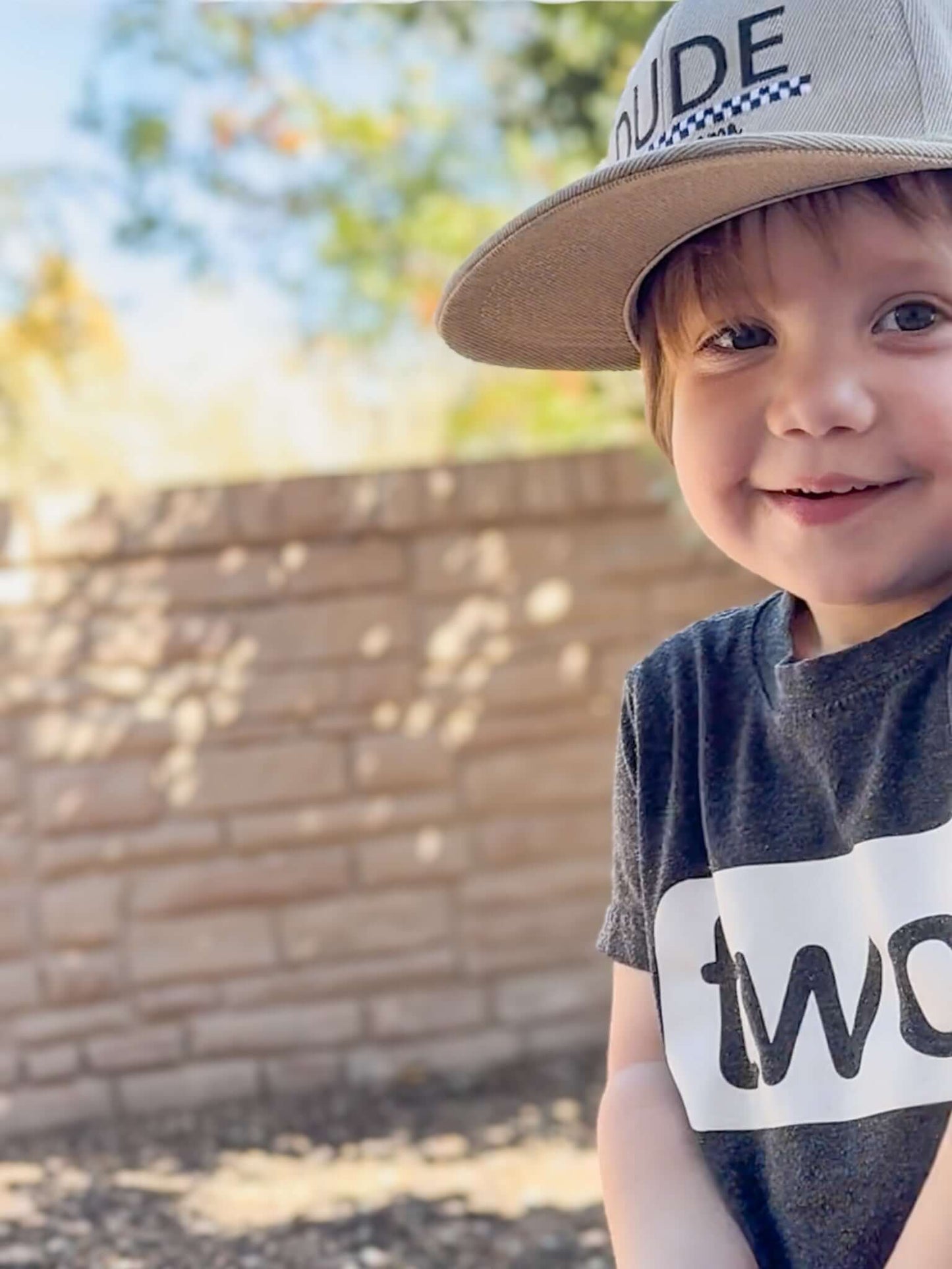 Smiling boy wearing a khaki Dude hat and gray shirt, embodying confidence in his stylish boy hat.