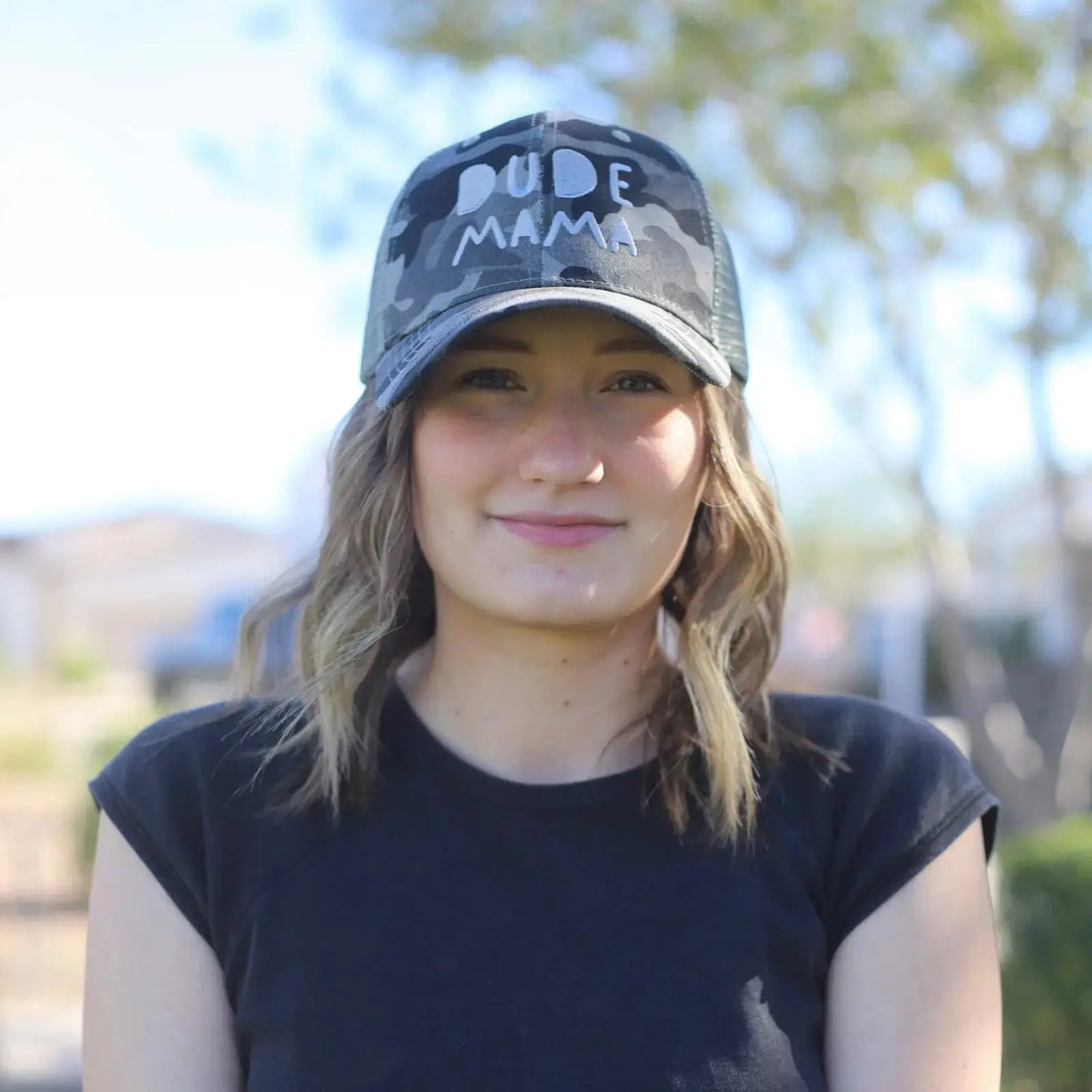 A woman wearing a Camo + Gray Dude Mama Hat, perfect for boy moms.