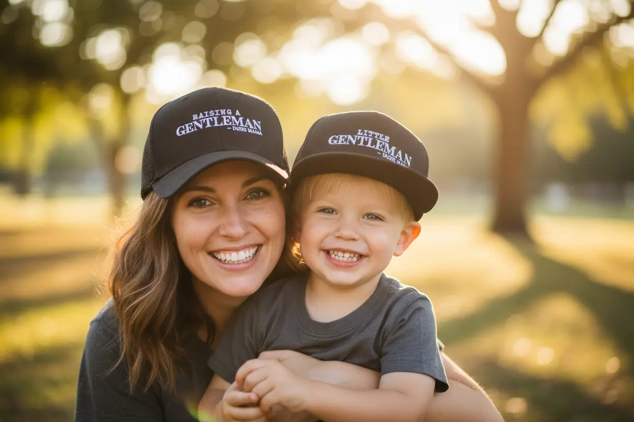 Mom and son outside wearing matching mom and son hats. Mama's hat says Raising a Gentleman and her son's hat says Little Gentleman.
