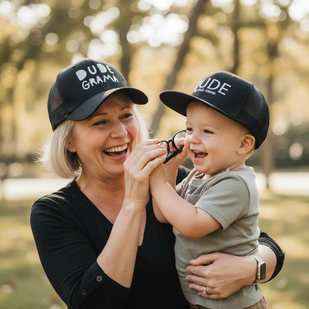 Grandma and Grandson wearing matching black hats. Grandma's hat says 'Dude Grama' and her grandson's hat says 'Dude'.