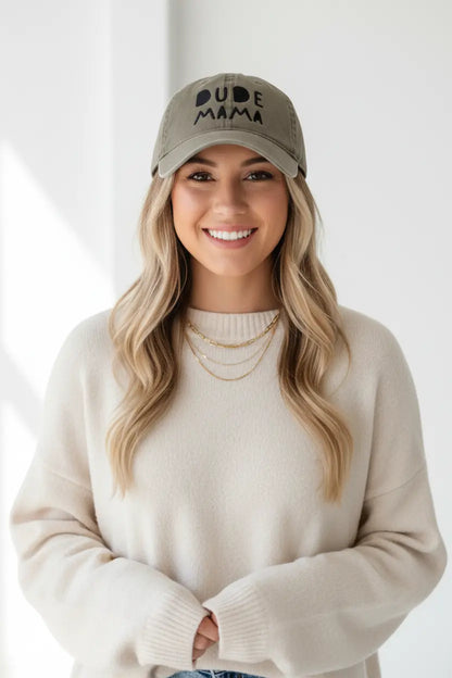 Mom smiling wearing a boy mom hat. It is an olive green hat and says 'Dude Mama'. It is a beautiful picture with a white background.