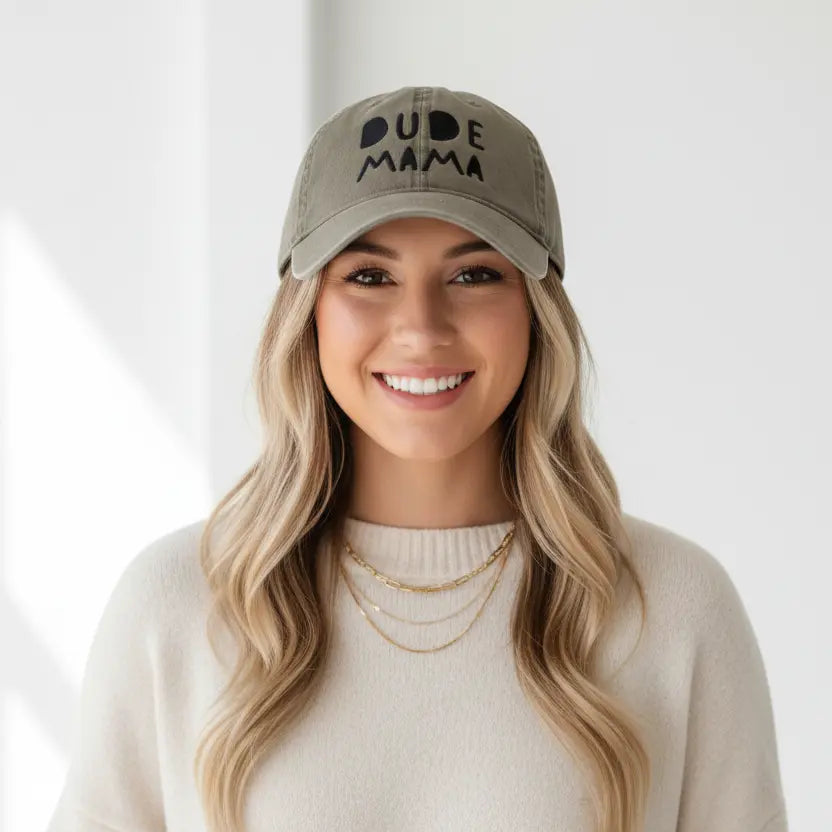 Mom smiling wearing a boy mom hat. It is an olive green hat and says 'Dude Mama'. It is a beautiful picture with a white background.