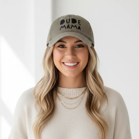 Mom smiling wearing a boy mom hat. It is an olive green hat and says 'Dude Mama'. It is a beautiful picture with a white background.