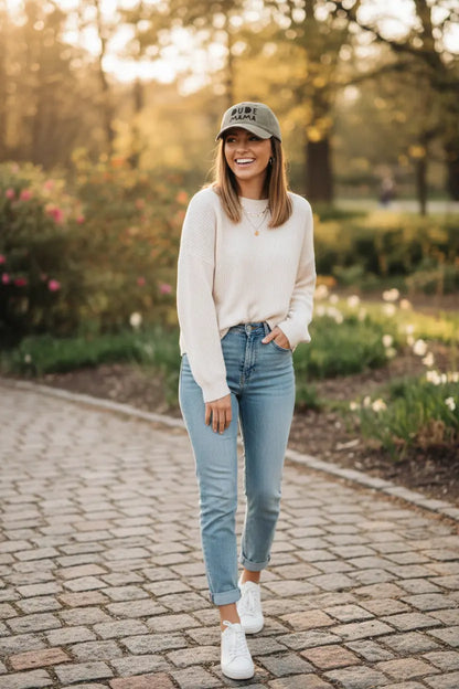 Mom smiling wearing a boy mom hat. It is an olive green hat and says 'Dude Mama'. It is a beautiful picture in a garden setting.